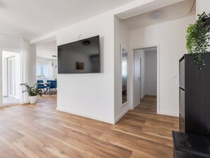 Ein modernes Wohnzimmer mit Flachbildfernseher, Holzboden und einem Essbereich mit blauen Stühlen.