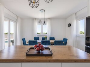 A modern kitchen with a wooden island, blue chairs, and a dining table with a view of greenery outside. - Vila Nik by Interhome (Zadar/Sukošan)