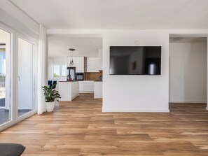 Eine moderne Küche mit Flachbildfernseher, Holzboden und einer Glastür zum Außenbereich.