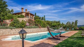 A swimming pool with a hammock, stone wall, and a building with chimneys.