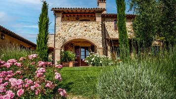 Un edificio in pietra con un arco centrale, circondato da un giardino curato con rose rosa e graminacee alte.