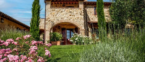 A stone building with a central archway, surrounded by a well-maintained garden with pink roses and tall grasses.