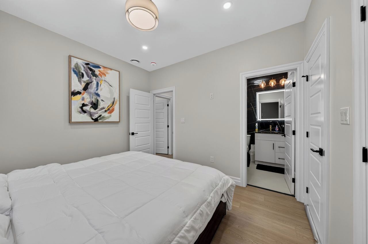 Una camera da letto con un letto grande, una lampada a soffitto, una porta che conduce al bagno e un quadro astratto appeso alla parete.