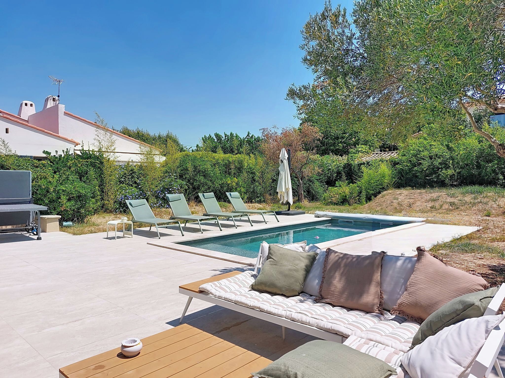 A poolside area with lounge chairs, a sofa, and a barbecue grill.