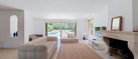 A modern living room with a large sectional sofa, a fireplace, and a view of a pool.
