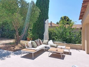 Un espace extérieur aménagé avec un canapé, deux petites tables d’appoint et une pergola.