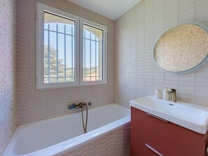 Un bagno con una vasca, una finestra e uno specchio tondo.