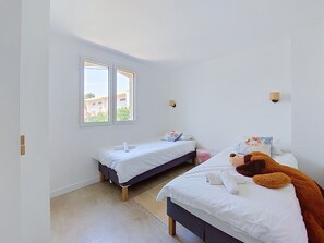 Camera da letto con due letti, un'ampia finestra e vista sugli edifici esterni.