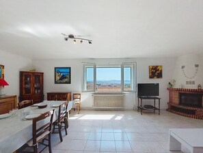 Ein geräumiger Wohnbereich mit Esstisch, Stühlen, Kamin, Fernseher und einem großen Fenster mit Blick auf die Landschaft.
