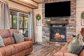 A cozy living room with a stone fireplace, a flat-screen TV, and a comfortable sofa. - NEW! Tall Timbers! Private Indoor Pool! (Hollister)