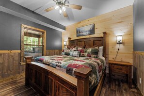 Een slaapkamer met een houten bed, een raam met zonwering, een plafondventilator, een nachtkastje en een wandlamp.