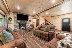 A cozy living room with a stone fireplace, wooden walls, and a comfortable seating area. - NEW! Tall Timbers! Private Indoor Pool! (Hollister)