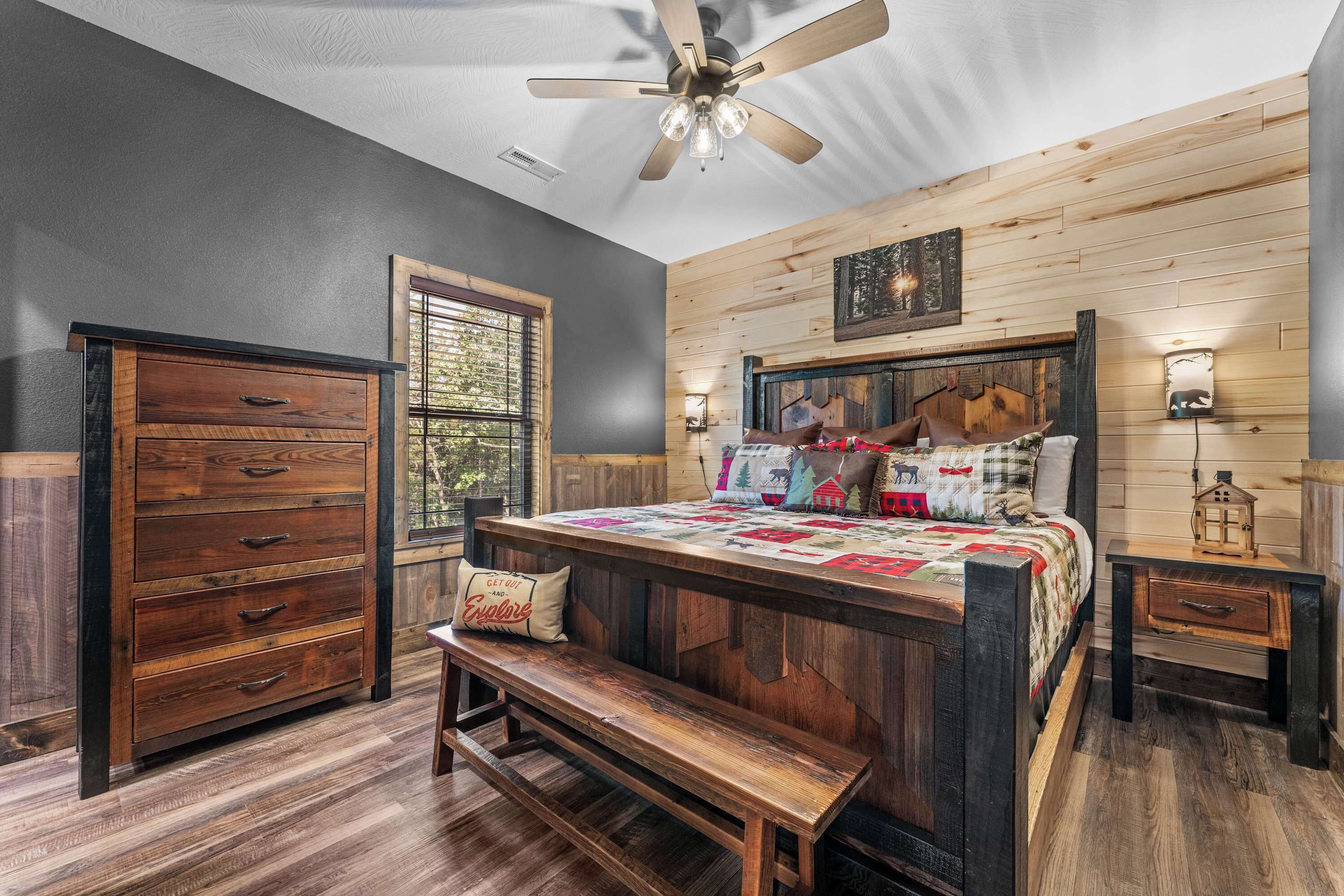 Une chambre à coucher avec une tête de lit en bois, un lit recouvert d’une courtepointe, une commode en bois, un banc et un ventilateur de plafond.
