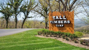 Et træskilt for Tall Timbers Camp med udsigt til træer og en vej i baggrunden.