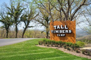 A wooden sign for Tall Timbers Camp with a view of trees and a road in the background. - NEW! Tall Timbers! Private Indoor Pool! (Hollister)
