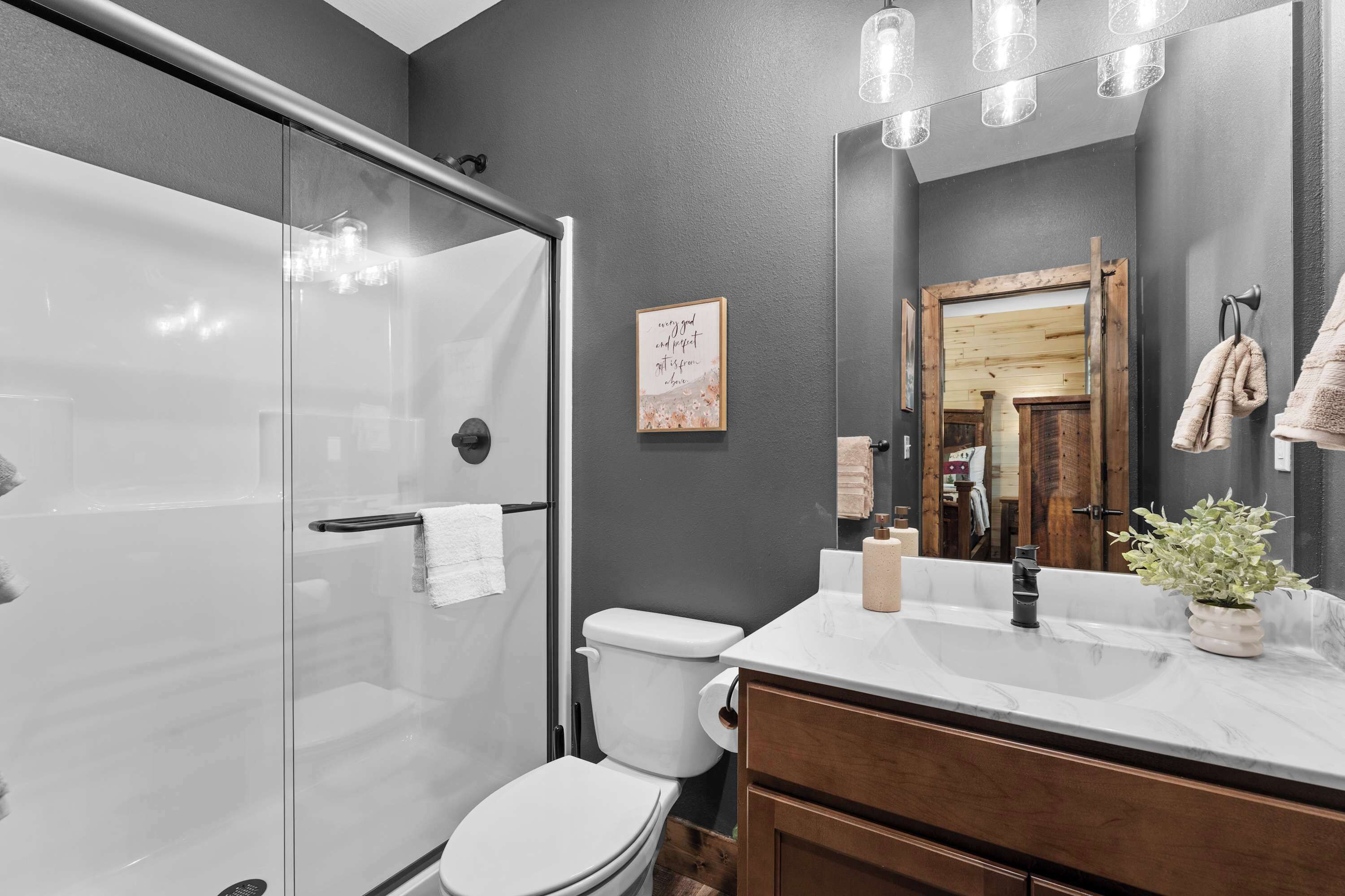 A modern bathroom with a glass shower enclosure, a white toilet, a wooden vanity, and a large mirror.