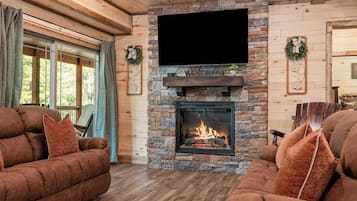 A cozy living room with a fireplace, wooden furniture, and a large TV mounted above it.
