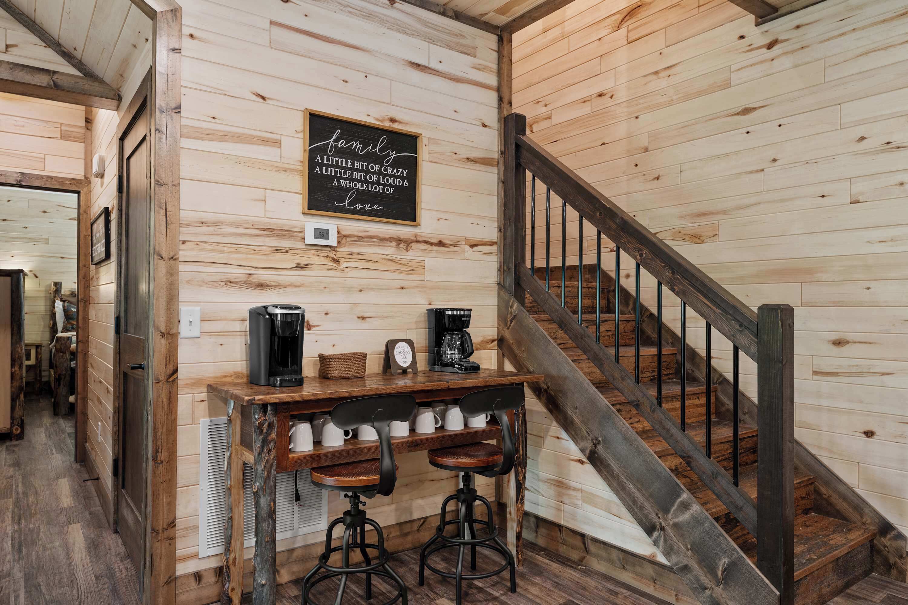 A wooden interior with a staircase, a coffee station with two bar stools, and a sign on the wall.