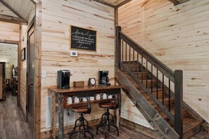 Interior de madera con una escalera, una estación de café con dos taburetes altos y un letrero en la pared.