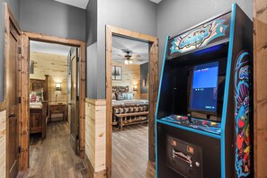 A room with a wooden floor, a bed with a headboard, a wooden bench, and a ceiling fan. - NEW! Private Indoor Pool! Hot Tub! Tall Timbers! (Hollister)