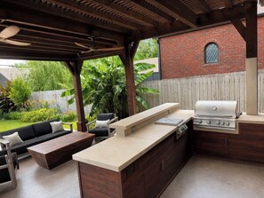 An outdoor kitchen with a grill, a wooden table, and a sofa.