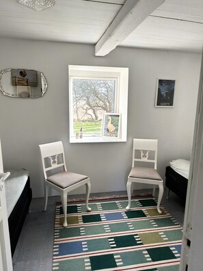 Um quarto com duas cadeiras brancas, um tapete estampado, um quadro de um galo e um quadro com texto.