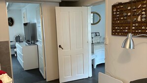 A room with a white door, a round rug, a grey sofa, and a wall-mounted lamp. - Enjoy island life in a Sejerø holiday home (Sejerø)