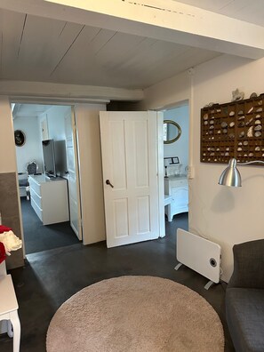 Um quarto com porta branca, um tapete redondo, um sofá cinza e uma luminária na parede.