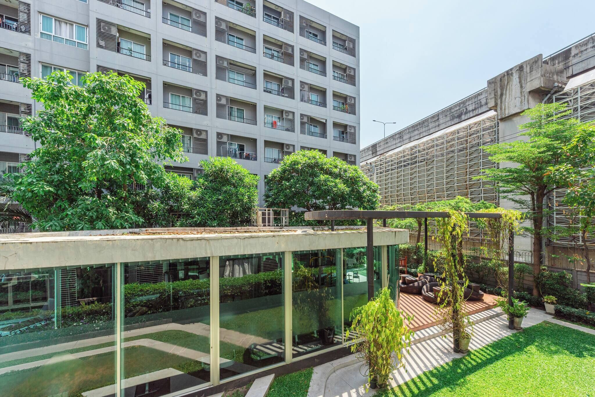 A modern building with a glass facade, outdoor seating area, and surrounding greenery.