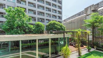 A modern building with a glass facade, outdoor seating area, and surrounding greenery.