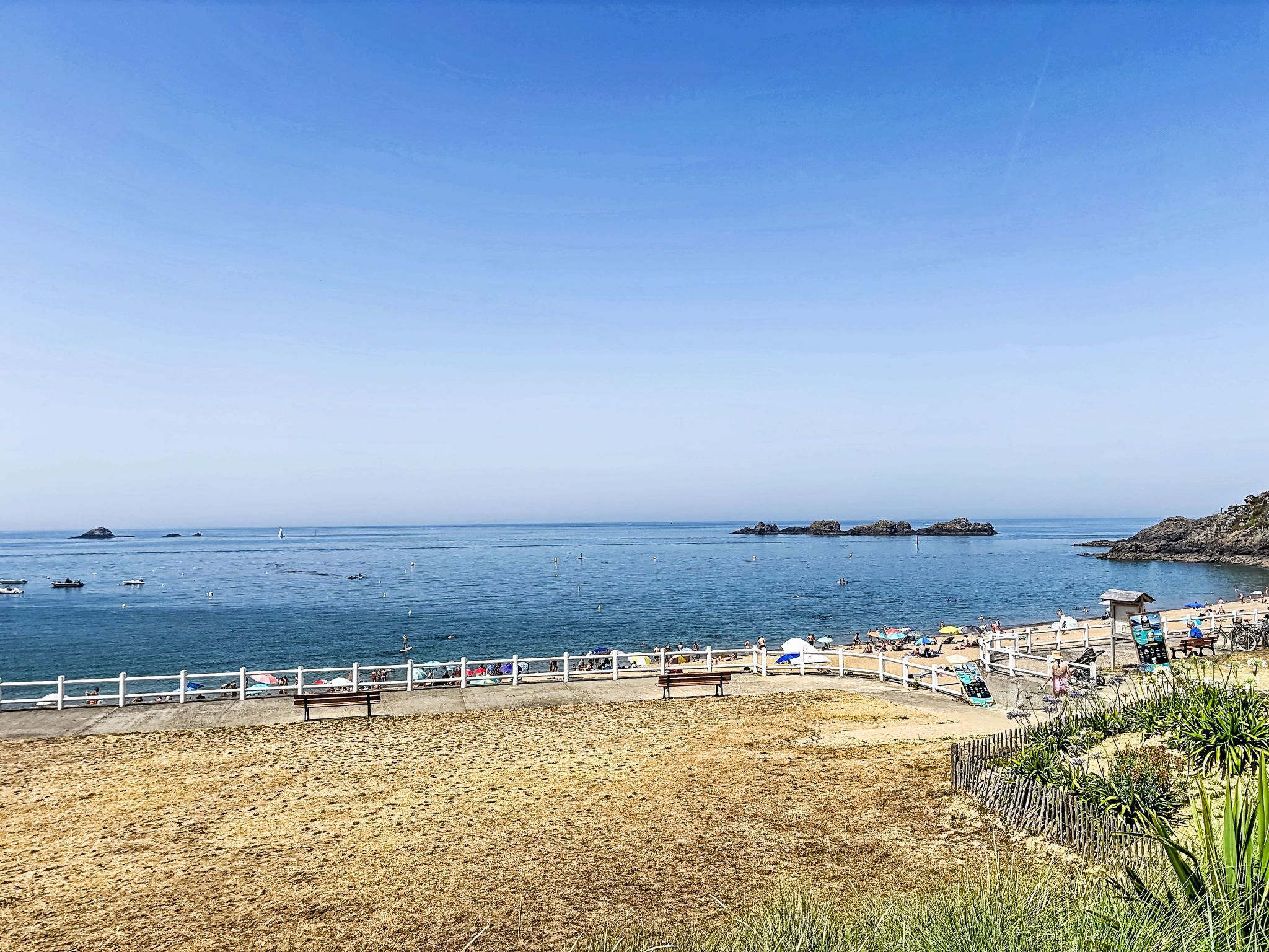 Een strand met een zandstrand, een houten hek en een helderblauwe lucht.