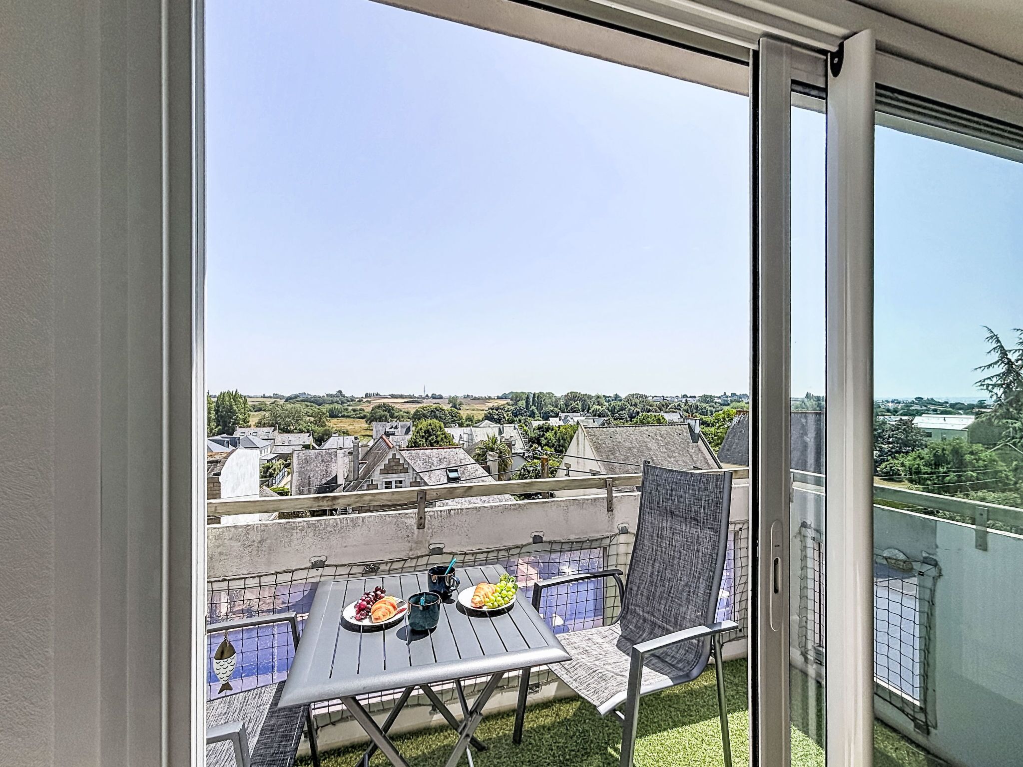 A balcony with a table set for two, a chair, and a view of a cityscape.