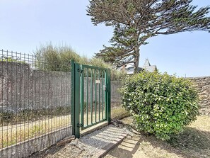 A gated entrance with a metal fence, a stone wall, and a large tree. - Résidence de la Mer by Interhome (Saint Malo)