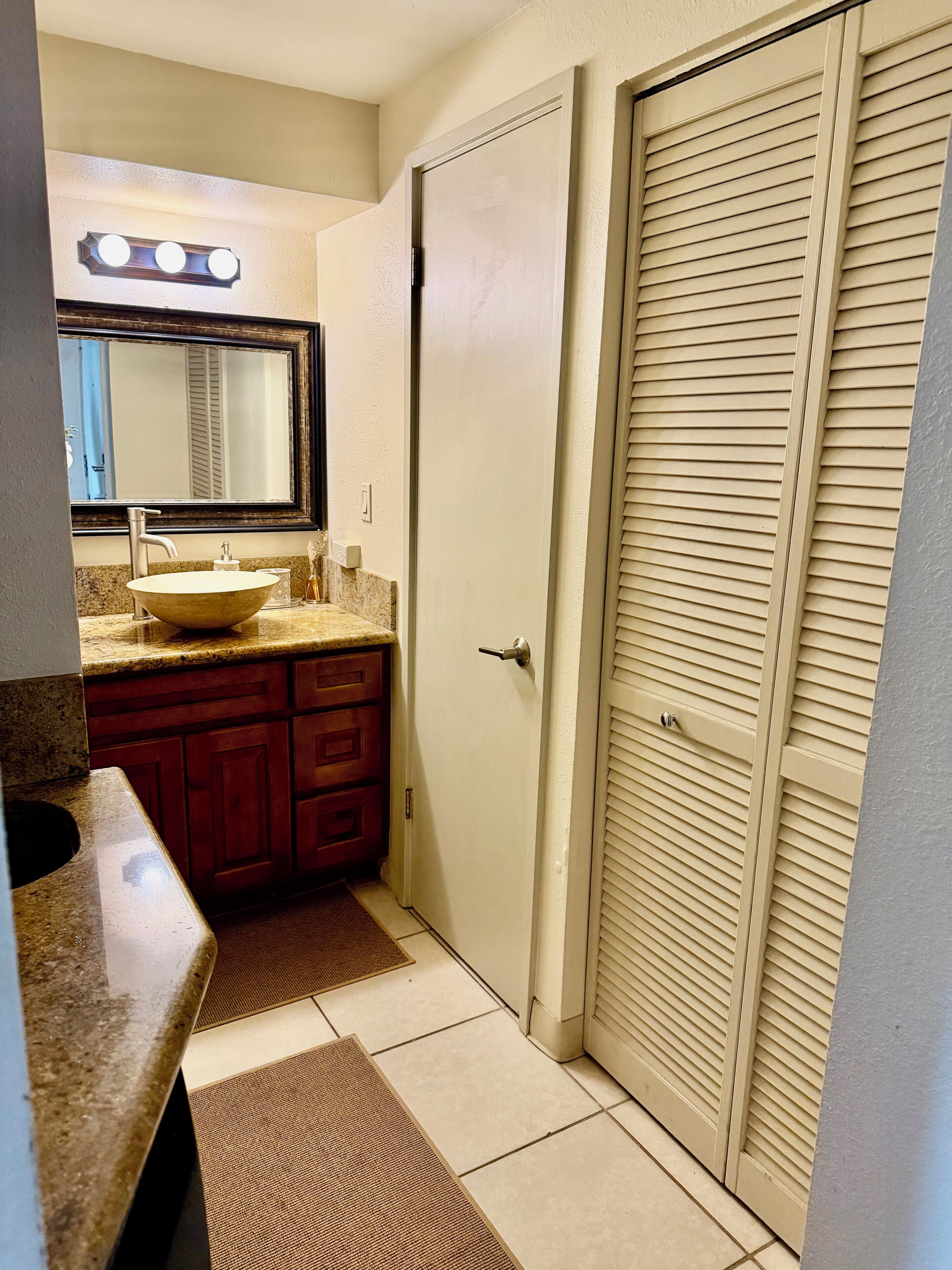 A bathroom with a sink, mirror, vanity, and a door.