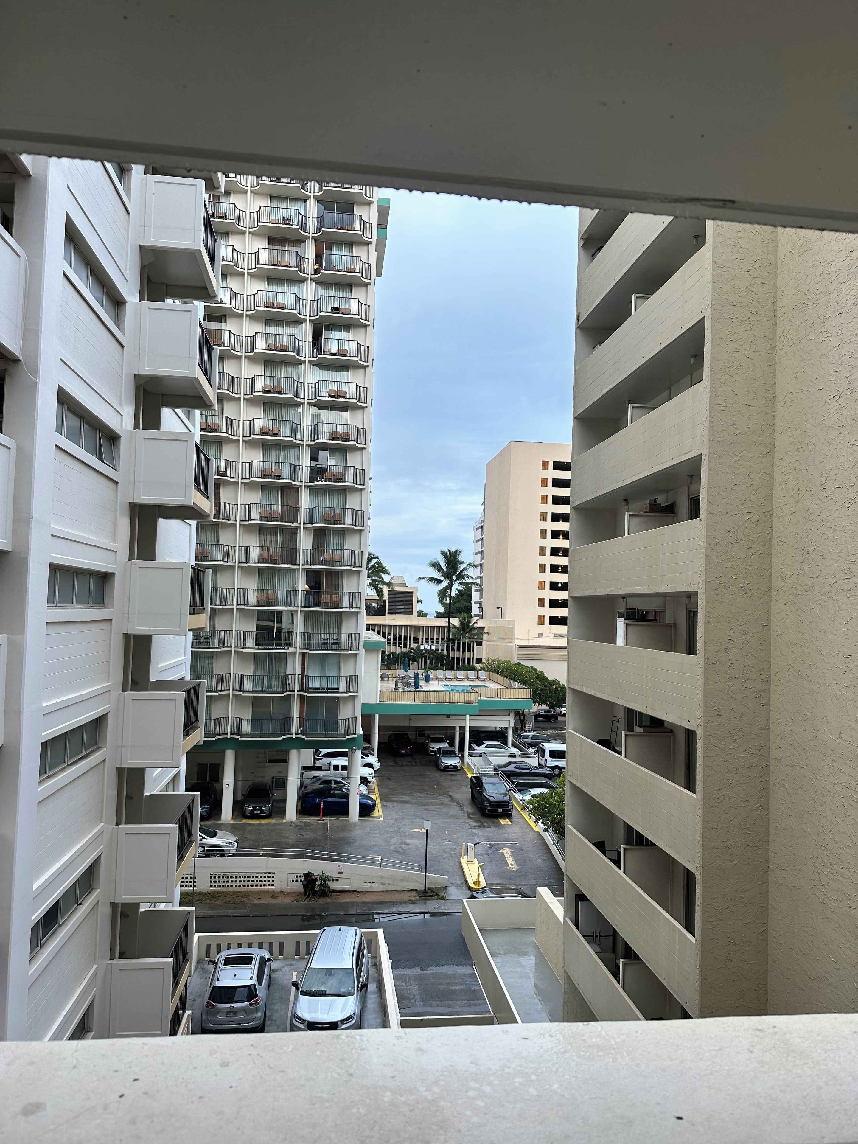 A multi-story parking garage with several cars parked, a covered outdoor area with a pool, and a view of adjacent buildings.