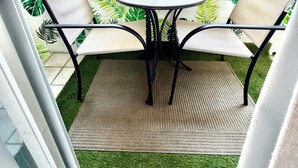 Ein Balkon mit einem runden Tisch, zwei Stühlen, einer kleinen Schildkrötchenfigur und einer Ziervase.