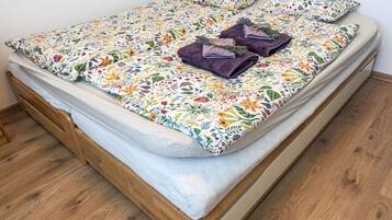 A bed with a floral bedspread, two purple towels, and a bouquet of flowers.