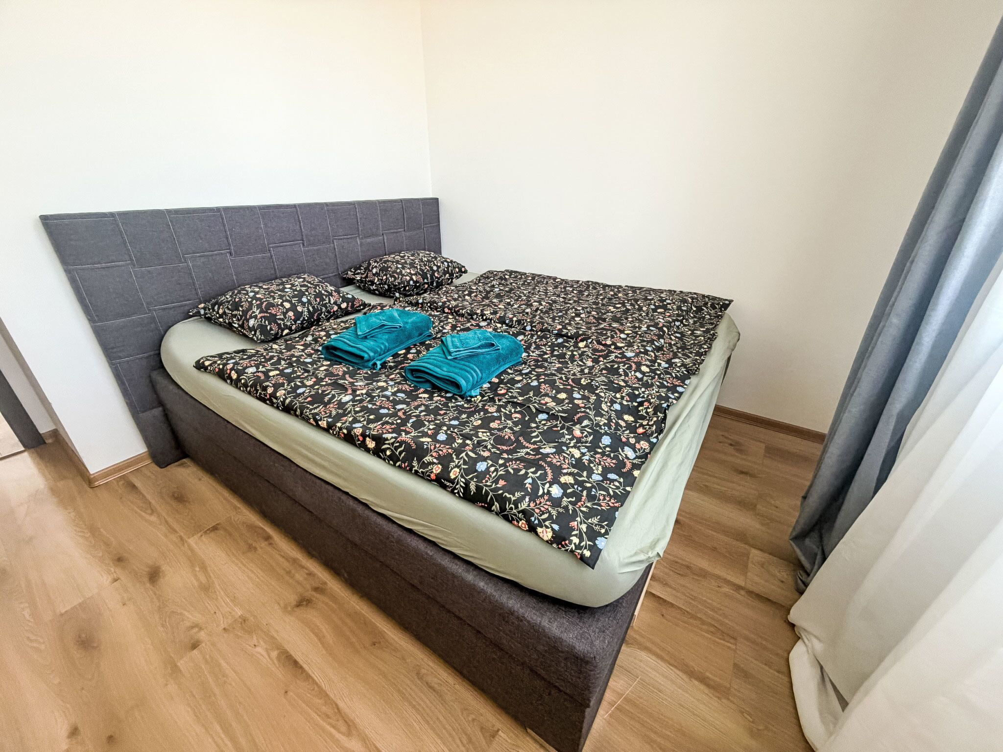 A bed with a floral bedspread, two teal towels, and matching pillows.
