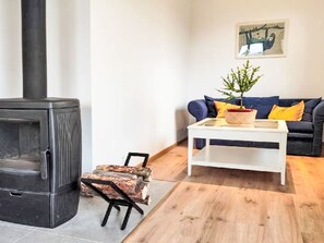 Una sala de estar con un estufa de leña negra, un sofá con cojines, una mesa de centro y un cuadro en la pared.