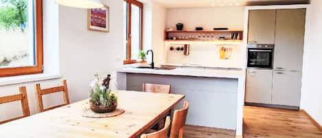 A modern kitchen with a wooden dining table, chairs, and a built-in oven.