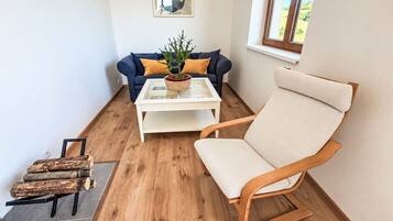A room with a blue sofa, a white coffee table, a wooden chair, and a window with a view of greenery.