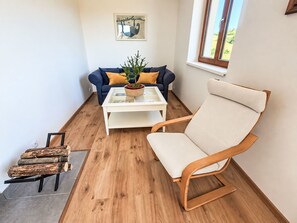 A room with a blue sofa, a white coffee table, a wooden chair, and a window with a view of greenery.