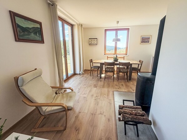 A room with a wooden floor, a dining table with chairs, a sofa, a fireplace, and a window with curtains.