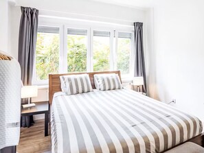 Une chambre d’hôtel avec un grand lit, deux tables de chevet, une fenêtre avec des rideaux et une vue sur la verdure.