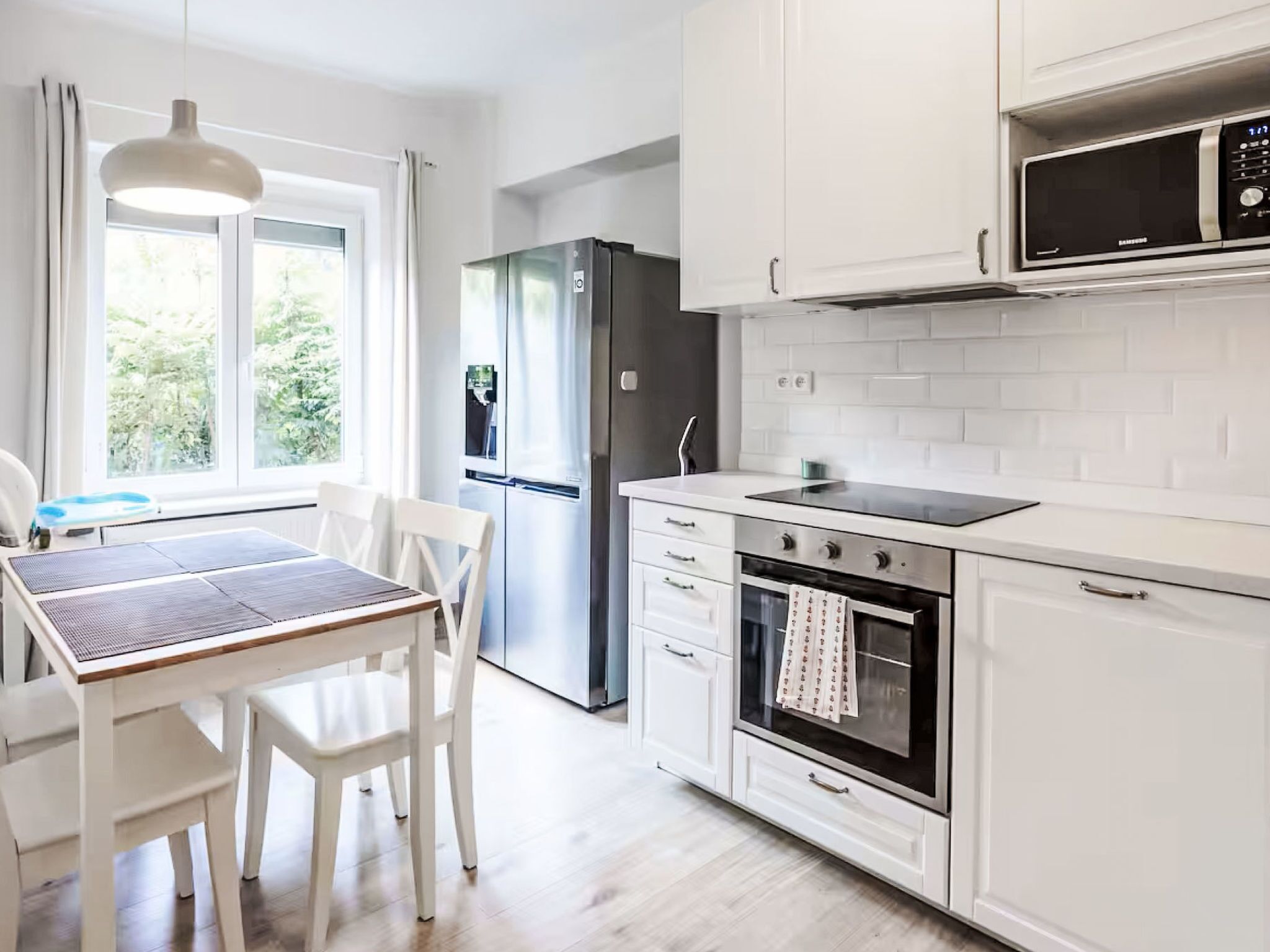 Una cucina moderna con mobili bianchi, forno integrato, microonde e frigorifero.
