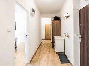 A narrow hallway with a wooden floor, a white cabinet, a black mat, and a wooden door. - Prague Castle Oasis by Interhome (Praha/6)