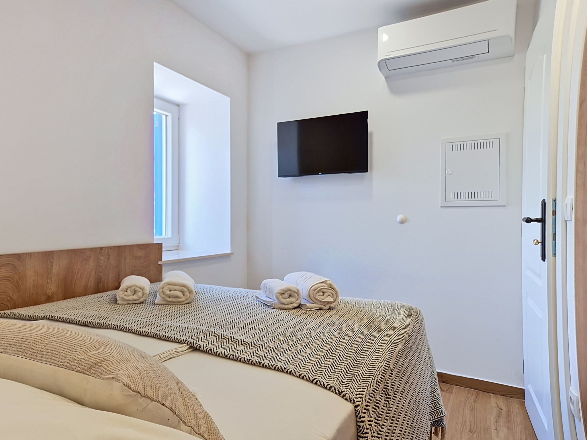 A hotel room with a bed, a TV, an air conditioning unit, and a window.