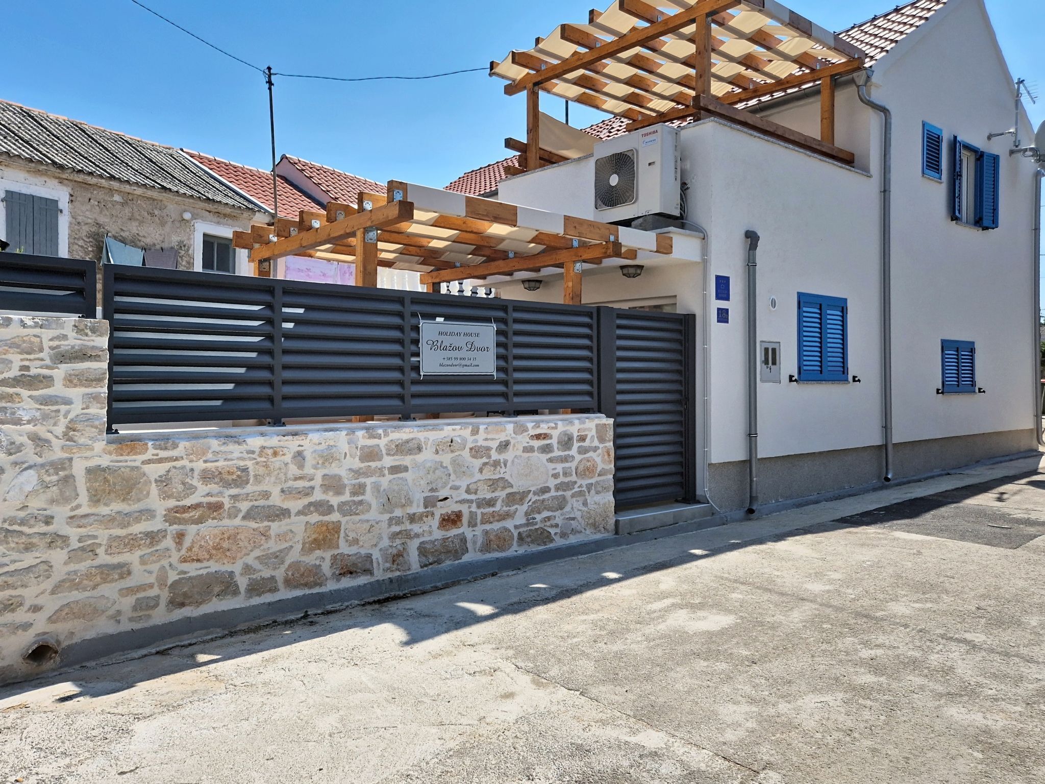 Une maison de vacances avec un mur en pierre, une pergola en bois et un portail en métal.
