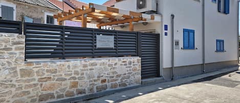 Une maison de vacances avec un mur en pierre, une pergola en bois et un portail en métal.