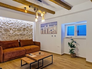 A living room with a stone wall, a brown sofa, a wooden coffee table, a hanging light fixture, and a window with blinds. - Blazov dvor by Interhome (Zaton)